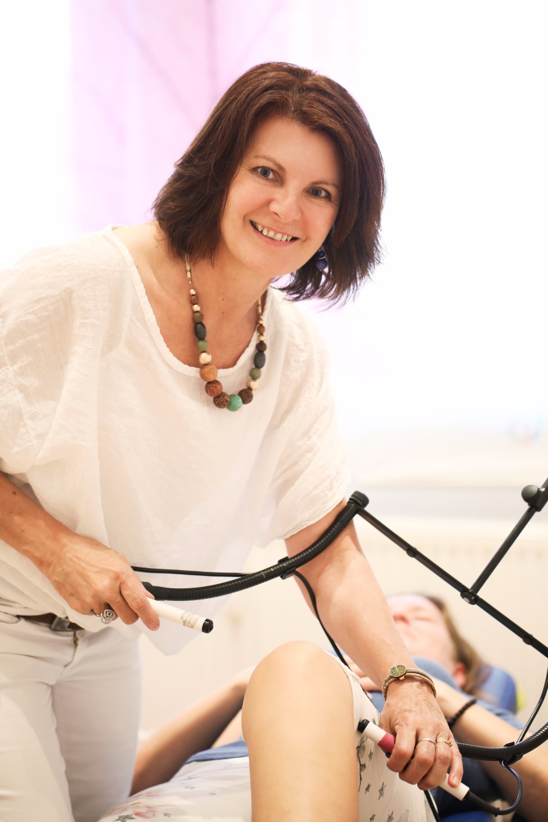 Heilpraktikerin Barbara Schütz behandelt das Knie einer liegenden Patientin mit Magnetfeldtherapie